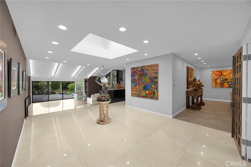Open great room flowing through floor-to-ceiling sliding glass to the pool yard, skylit ceiling, art on every wall
