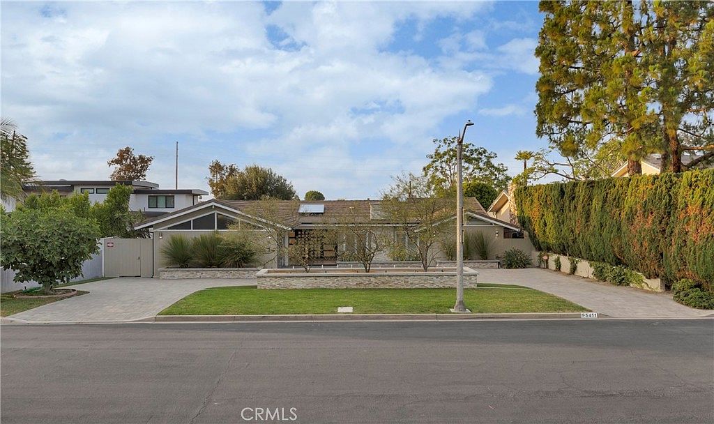 Daytime view of the front elevation showing the long horizontal ranch roofline, stone-clad walls, and central glass entry