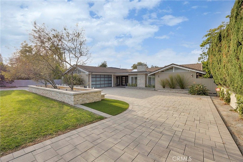 Front courtyard showing the paver driveway, raised stone planters, and the home's symmetrical ranch facade from the approach