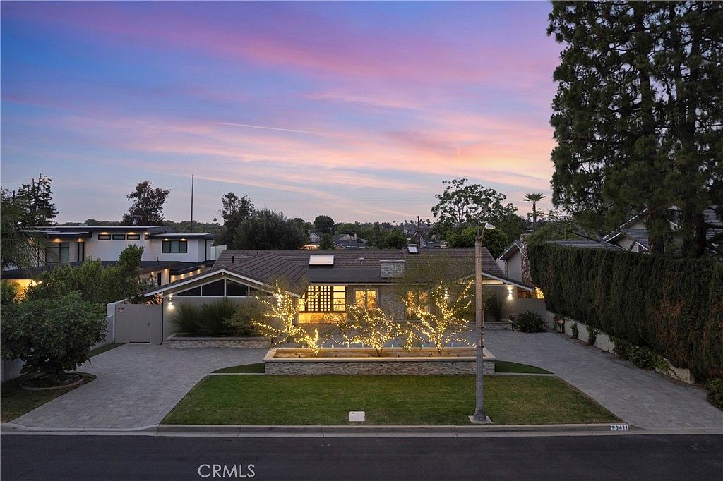 A single-story Park Estates ranch at twilight, strings of warm light wrapped through mature trees in the front garden under a pink dusk sky
